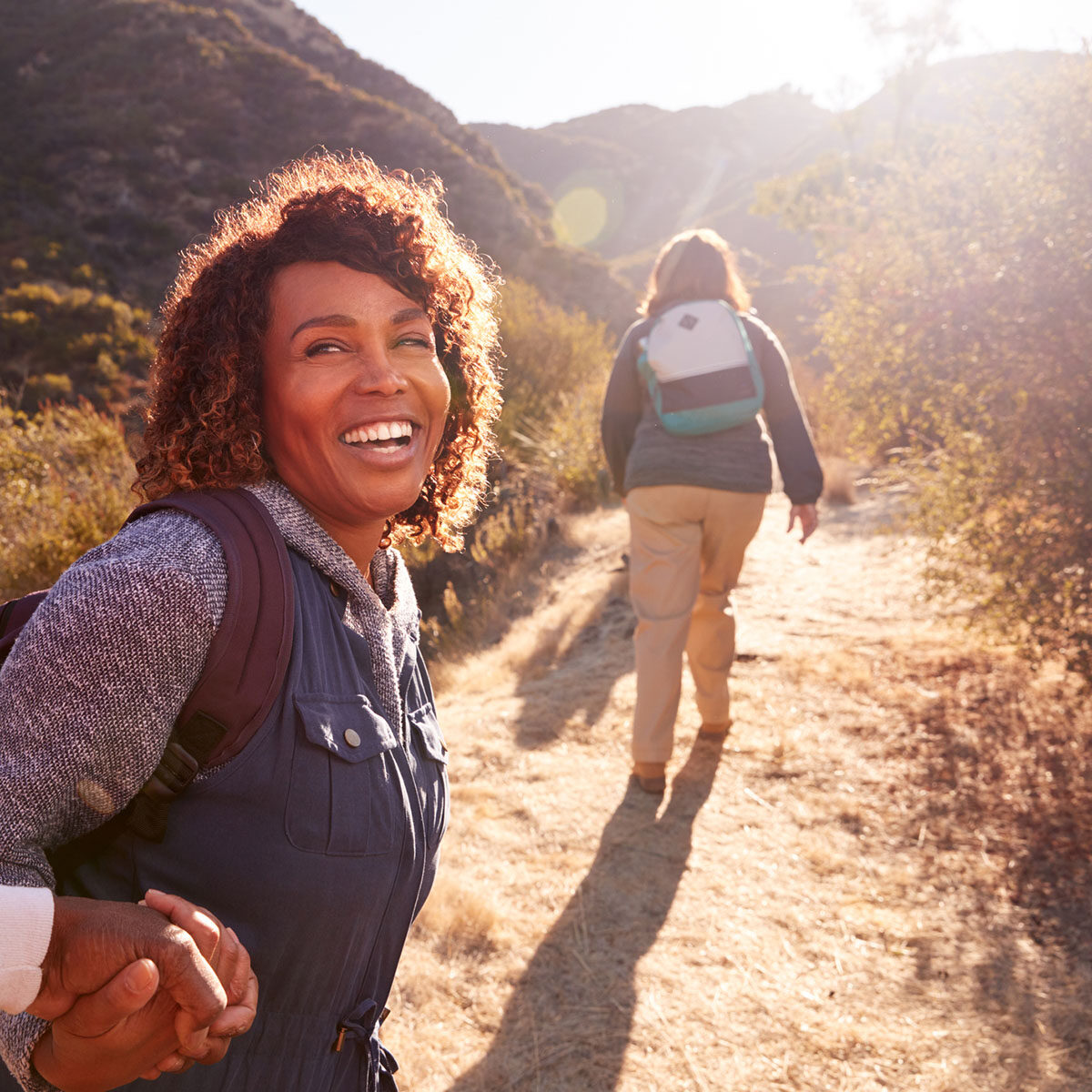 Woman Helping Man On Trail As Group Of Senior Friends Go Hiking In Countryside Together